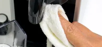 Ruka čistí kávovar hadříkem u výstupu.