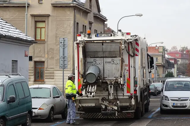Pracovník sběru odpadu u vozidla na ulici.
