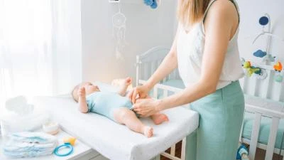 Žena mění miminko na přebalovacím pultu v světlé dětské místnosti.