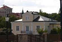 Fotografie Lumbeho vily s bílými okny za dřevěným plotem.