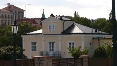 Fotografie Lumbeho vily s bílými okny za dřevěným plotem.