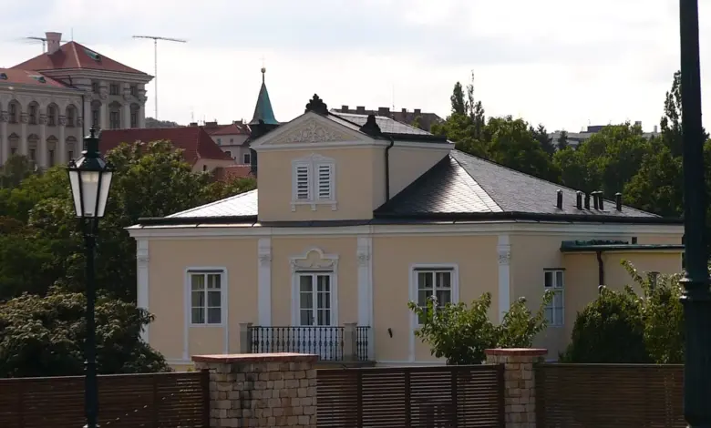 Fotografie Lumbeho vily s bílými okny za dřevěným plotem.