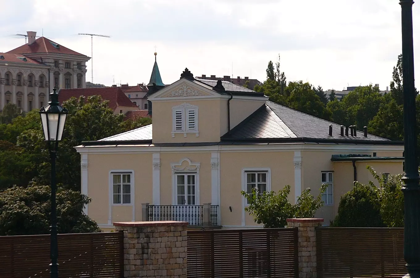 Fotografie Lumbeho vily s bílými okny za dřevěným plotem.