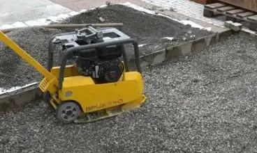 Žlutý vibrační deska na štěrku u zámkové dlažby.
