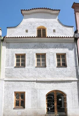 Bílá budova se šedými reliéfními vzory na fasádě ukazuje techniku sgraffita.