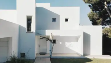 Bílá minimalistická vila s geometrickými okny a zahradou.