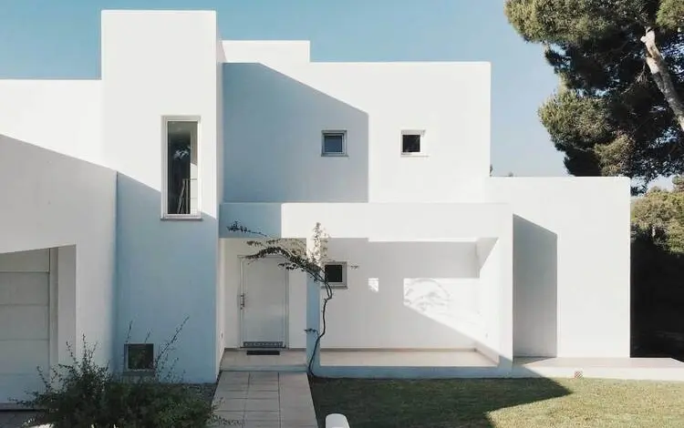 Bílá minimalistická vila s geometrickými okny a zahradou.