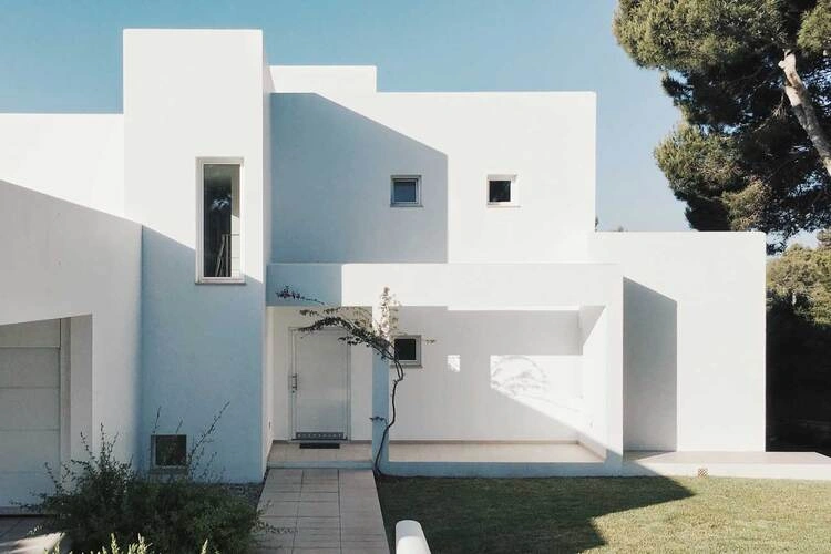 Bílá minimalistická vila s geometrickými okny a zahradou.