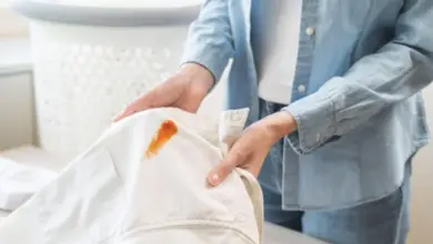 Osoba drží bílou košili s viditelnou olejovou skvrnou.