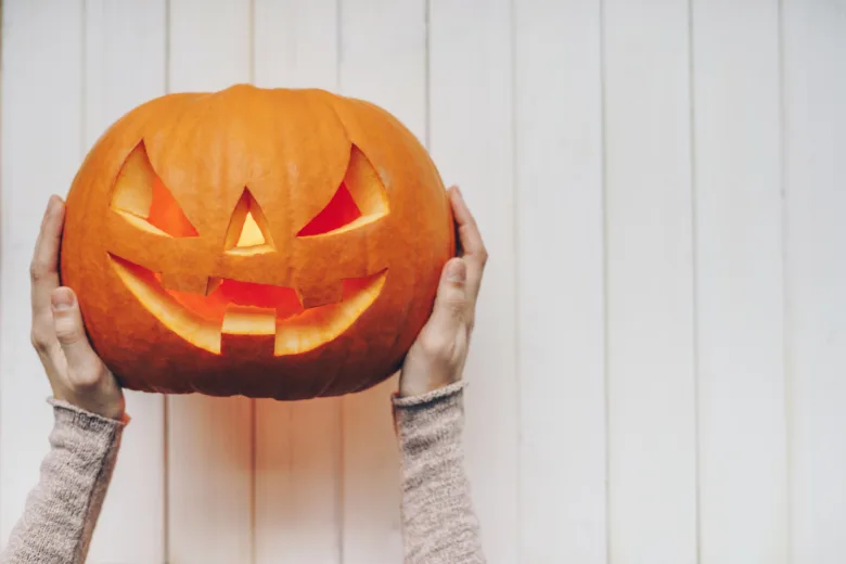 Ruce drží vyřezanou dýni na Halloween.