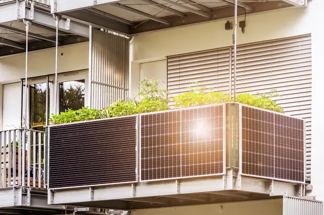 Fotografie fotovoltaických panelů na balkóně s rostlinami.