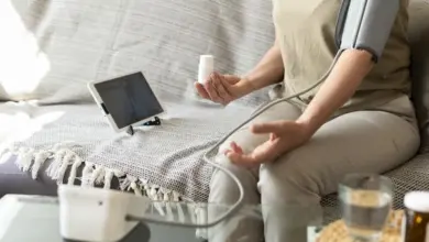 Žena měří krevní tlak doma s digitálním přístrojem.