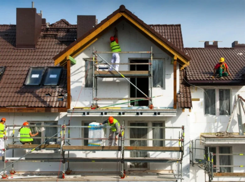 Stavební dělníci rekonstruují dům s novými okny a střechou.