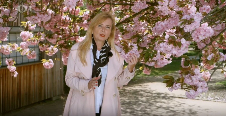 Žena stojí pod kvetoucí sakurou v zahradě.