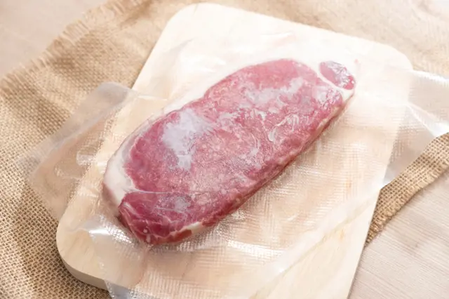 Frozen meat steak in vacuum pack on cutting board