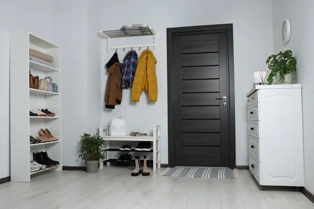 Elegantná chodba s bílými skříněmi, visící kabáty a rostlinami.