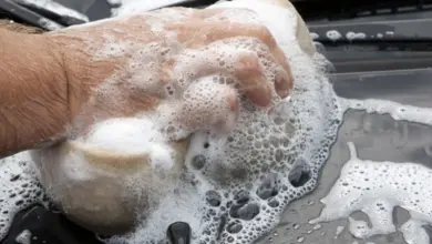 Ruka myje auto špongií plnou pěny.