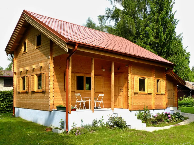 Dřevěná chatka s červenou střechou vhodná pro celoroční bydlení.