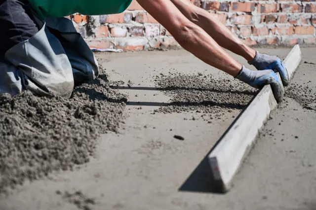 Stavebník vyrovnává suchý beton pomocí pravítka.