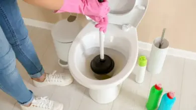 Člověk s růžovými rukavicemi opravuje ucpaný záchod pomocí hadice.