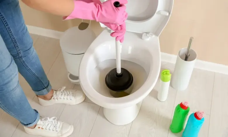 Člověk s růžovými rukavicemi opravuje ucpaný záchod pomocí hadice.