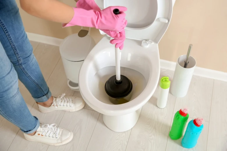 Člověk s růžovými rukavicemi opravuje ucpaný záchod pomocí hadice.