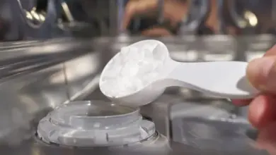 Ruka s lžičkou jedlé sodinky nad zásobníkem myčky nádobí.