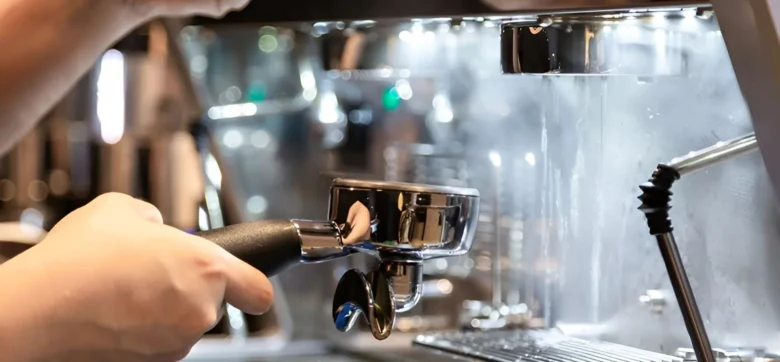 Barista čistí portafiltr pod hlavou kávovaru.