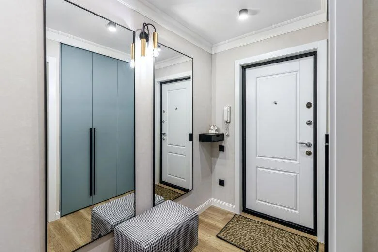 Moderní chodba s bílými dveřmi, zrcadlem a elegantním sedacím kusem.