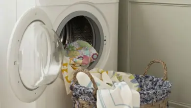 Bílá pračka s otevřenou dveřmi vedle košíku na prádlo.