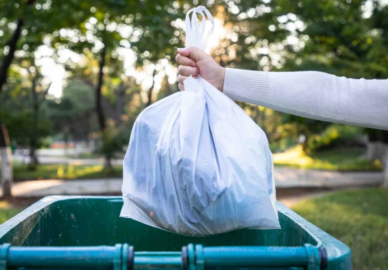 Hand holding trash bag over bin