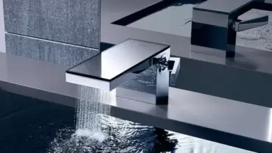 Moderní chromový kohout do vany s vodou tekoucí z plochého výstupu.
