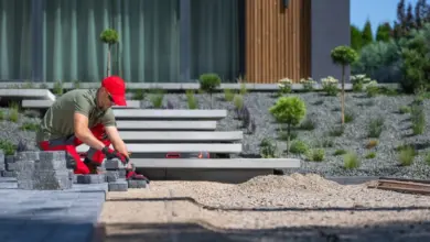 Muž staví kamenné schody pro terasu u moderního domu.