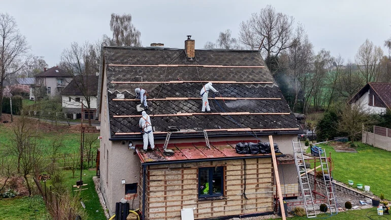 Pracovníci v ochranném obleku demontují starou střechu.
