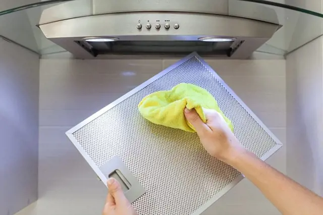 Ruční čištění sítě z tuků na digestoři žlutou utěrkou.