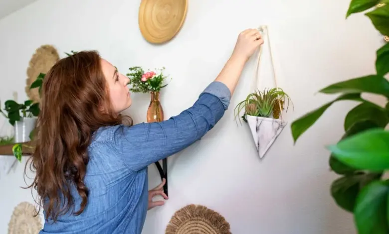 Žena zavěšuje rostlinu na zeď při úpravách interiéru.