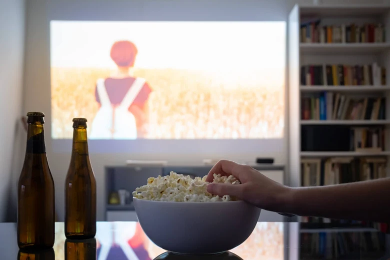 Domácí kino s projekcí na zeď, popcornem a pivy v popředí.