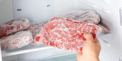 Ruka drží balení mraženého masa v otevřeném mrazáku.