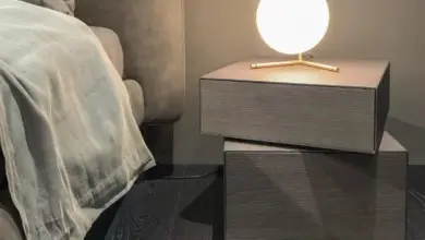 Moderní dřevěný noční stolek s lampačkou vedle postele.
