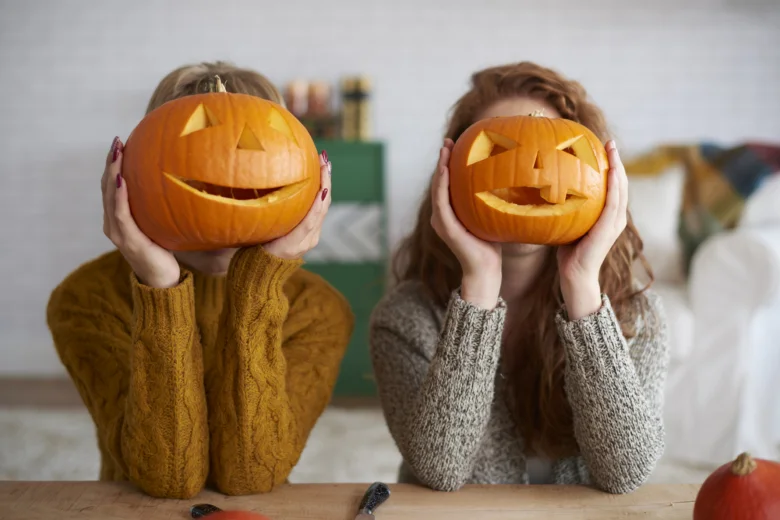 Dvě dívky drží před obličejem vydlabané dýně na Halloween.