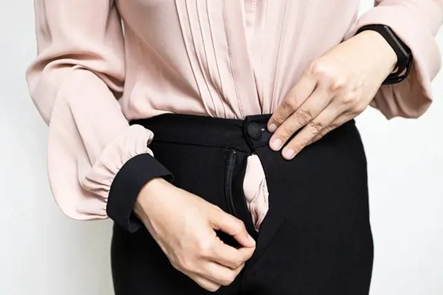 Žena opravuje rozbitý zip na černých kalhotách.