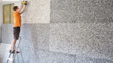 Muž na žebříku montuje akustické panely přímo na stěnu v bytě.