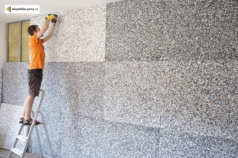 Muž na žebříku montuje akustické panely přímo na stěnu v bytě.