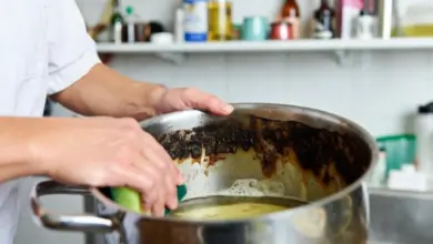 Člověk čistí připálený hrnec zelenou houbou v kuchyni.