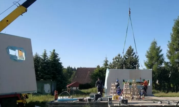 Stavebníci montují prefabrikovaný dům s pomocí kranu.