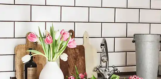 Bílá váza s růžovými tulipány na kuchyňském pultu.